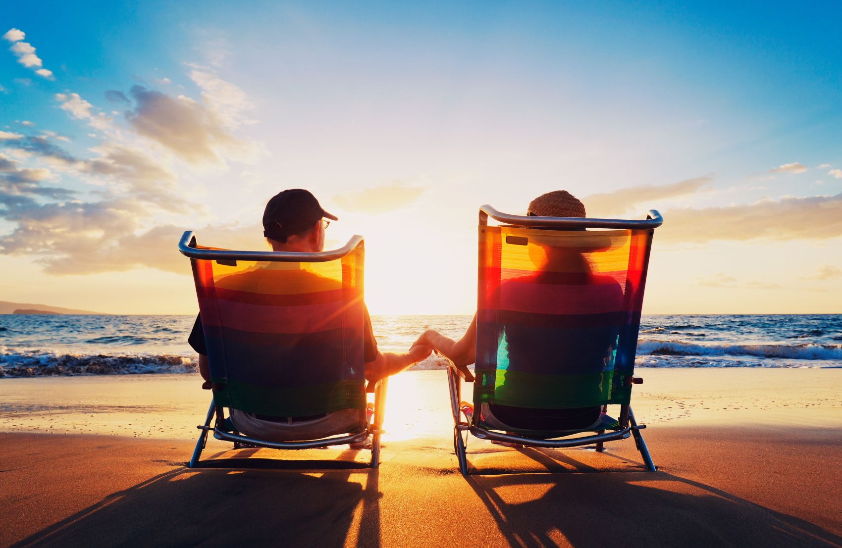 Couple sitting on beach chairs, holding hands watching sunrise on a beach