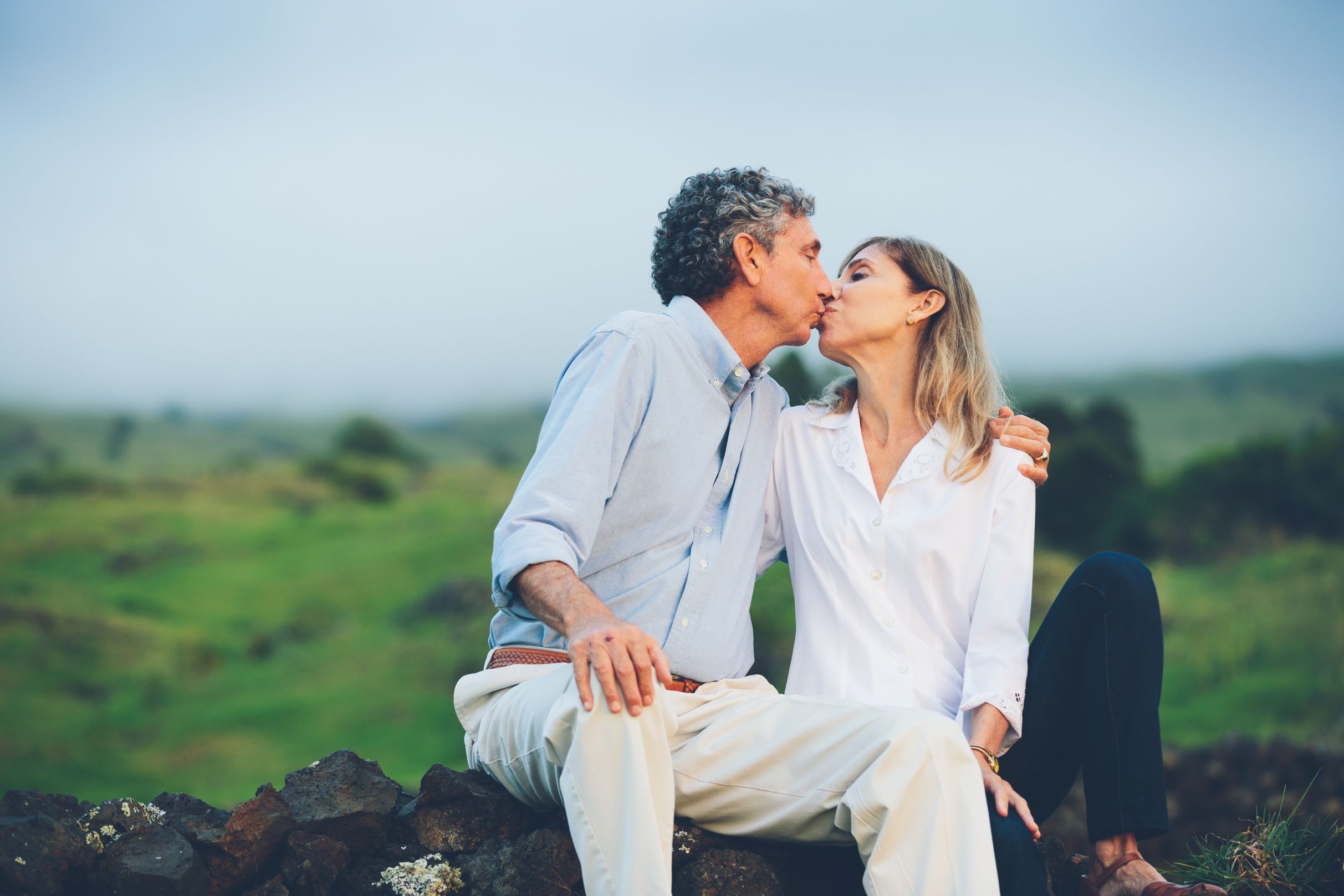 Couple sitting on a stone wall in green field and kissing