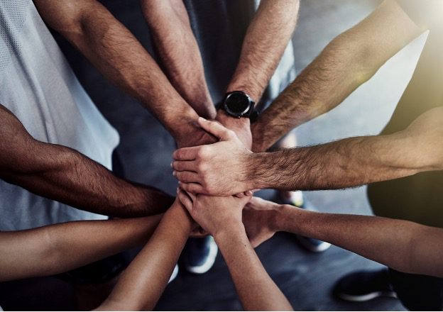 Circle of men with hands grouped together in the middle - featured image for Group Coaching